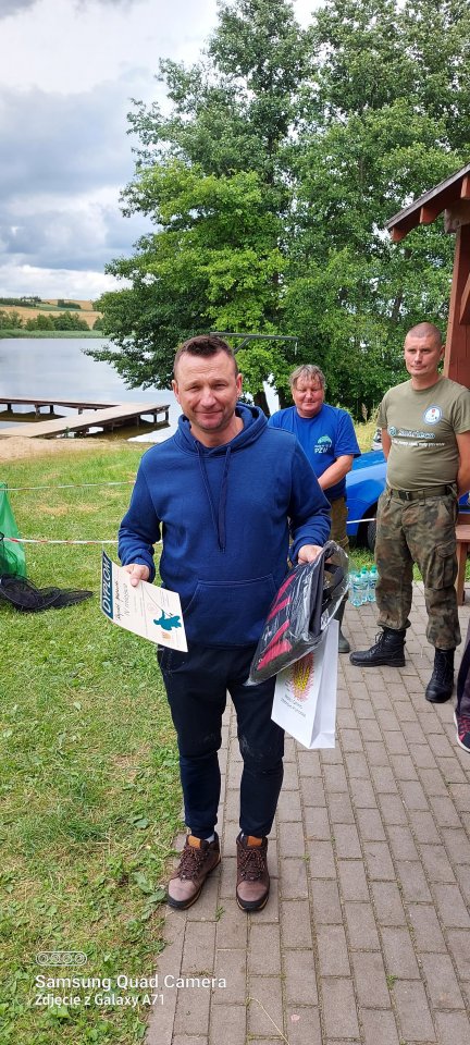 Zawody wędkarskie Uczestnik zawodów wędkarskich z nagrodami i dyplomem w rękach.