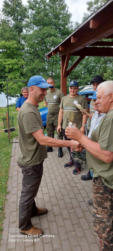 Zawody wędkarskie Uśmiechnięty zawodnik odbiera nagrodę za udział w zawodach wędkarskich.