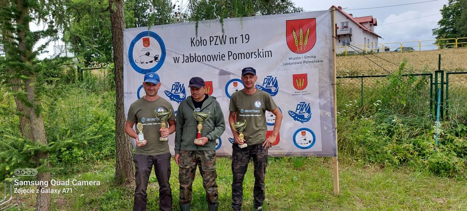Zawody wędkarskie Laureaci zawodów z nagrodami na tle banneru.