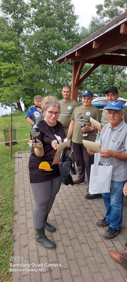 Zawody wędkarskie grupa zawodników z nagrodami w rękach.