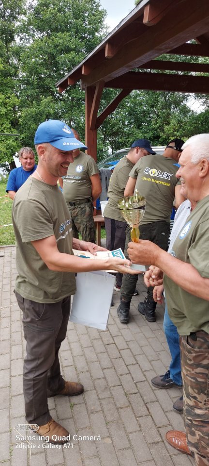 Zawody wędkarskie uśmiechniety zawodnik odbiera nagrodę za udział w zawodach wędkarskich