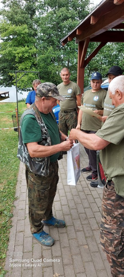Zawody wędkarskie zawodnik z wędką odbiera nagrodę.