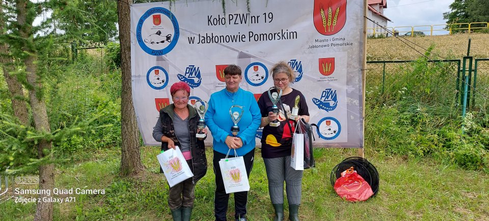 Zawody wędkarskie Laureatki zawodów z nagrodami na tle banneru.