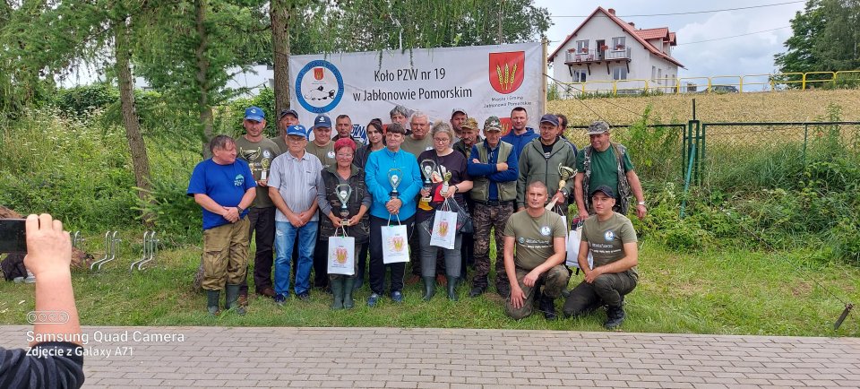 Zawody wędkarskie wszyscy uczestnicy zawodów na tle banneru.